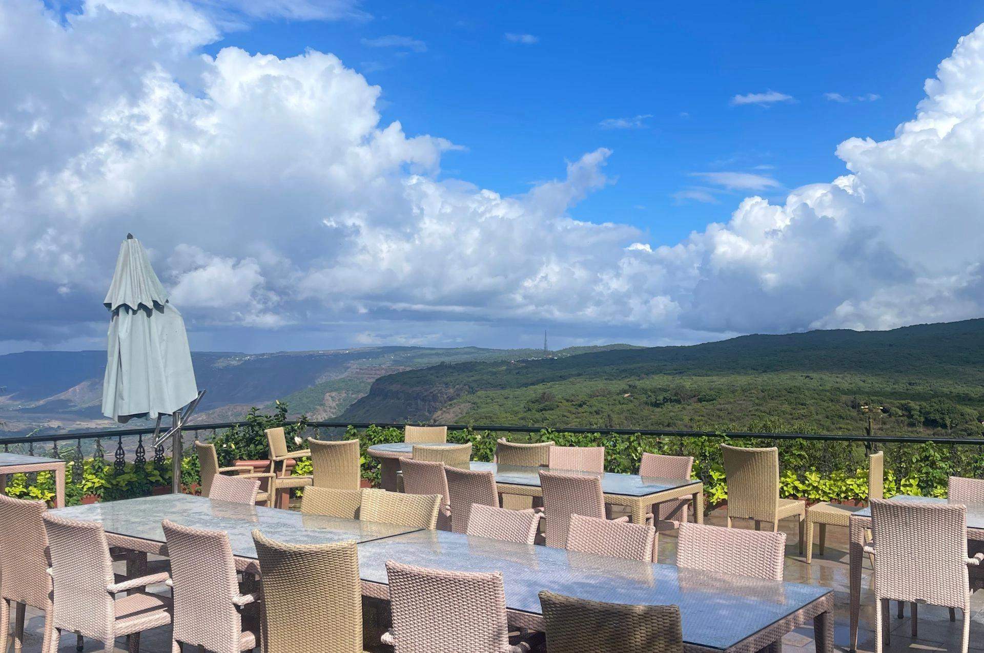 Outdoor seating area on a pool deck with panoramic views of the valley under a bright blue sky.